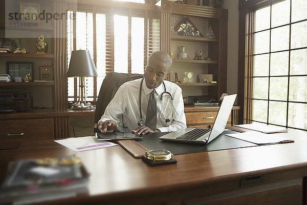 Schwarzer Arzt benutzt digitales Tablet im Büro