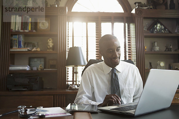 Schwarzer Arzt benutzt Laptop im Büro