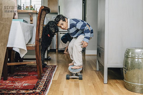 Gemischtrassiger Junge fährt Skateboard in der Küche