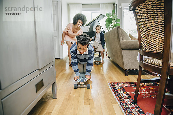 Gemischtrassige Familie beobachtet Junge beim Skateboardfahren im Wohnzimmer