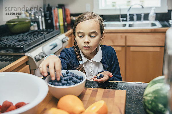 Gemischtrassiges Mädchen pflückt Blaubeeren aus einer Schüssel in der Küche