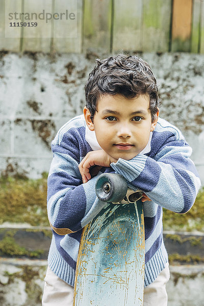 Gemischtrassiger Junge  der sich im Freien auf ein Skateboard stützt