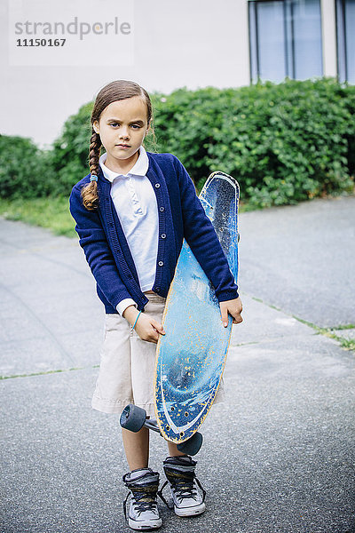 Gemischtrassiges Mädchen hält Skateboard auf dem Gehweg