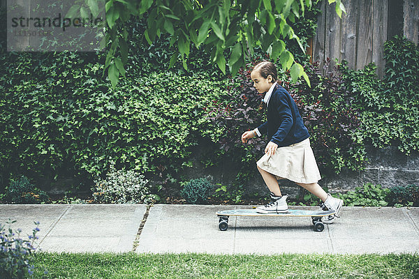 Gemischtrassiges Mädchen fährt Skateboard auf dem Bürgersteig