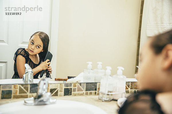 Gemischtrassiges Mädchen beim Bürsten der Haare im Badezimmer