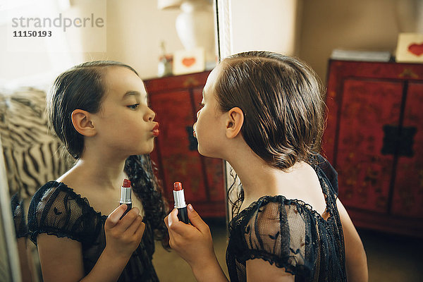 Gemischtrassiges Mädchen trägt Lippenstift im Spiegel auf