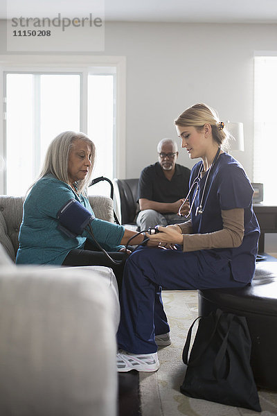 Krankenschwester misst Blutdruck eines Patienten im Wohnzimmer