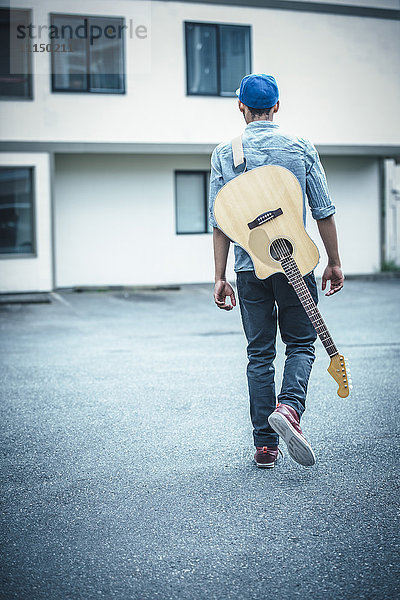 Gemischtrassiger Junge mit Gitarre auf einem Parkplatz