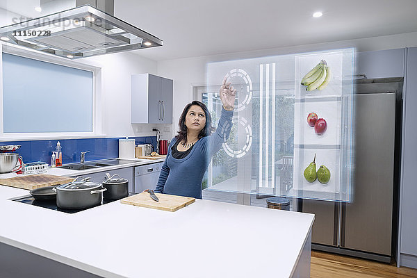 Gemischtrassige Frau mit holografischem Bildschirm in der Küche