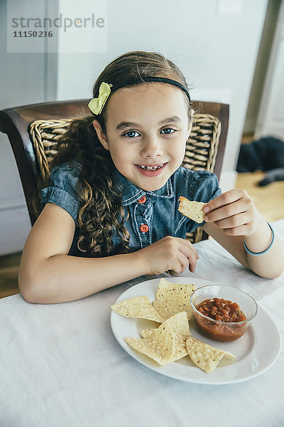 Gemischtrassiges Mädchen isst Chips und Salsa am Tisch