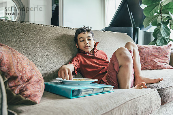 Gemischtrassiger Junge isst Snack auf Sofa