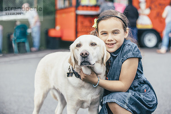 Gemischtrassiges Mädchen umarmt Hund auf der Straße