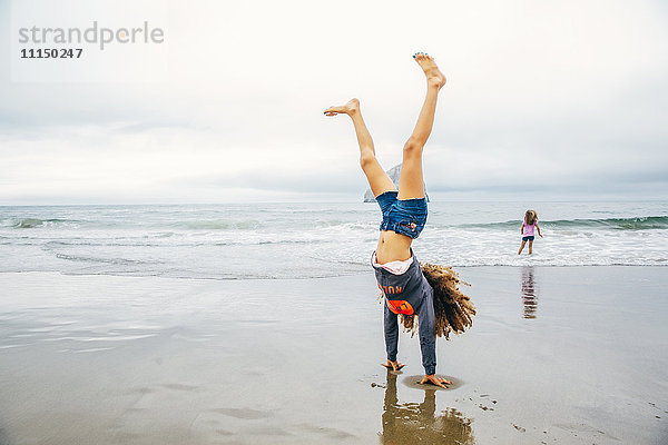 Gemischtrassiges Mädchen macht Handstand am Strand