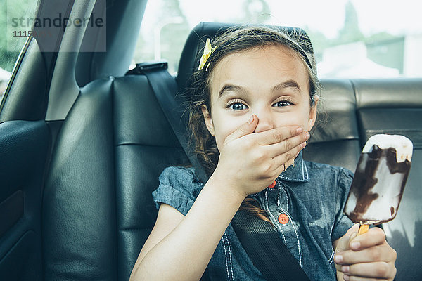Gemischtrassiges Mädchen isst Eiscreme-Riegel auf dem Rücksitz eines Autos