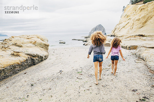 Gemischtrassige Schwestern gehen am Strand spazieren