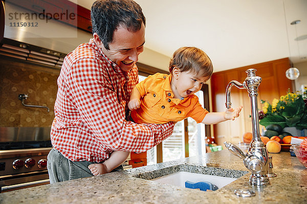 Vater und Sohn spielen mit dem Wasserhahn in der Küche