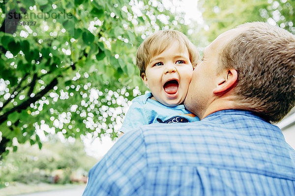 Vater küsst Wange seines kleinen Sohnes im Freien
