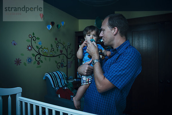 Vater gibt Baby Sohn Schnuller im Kinderzimmer