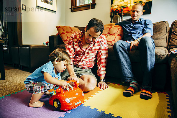 Schwule Väter spielen mit ihrem kleinen Sohn im Wohnzimmer