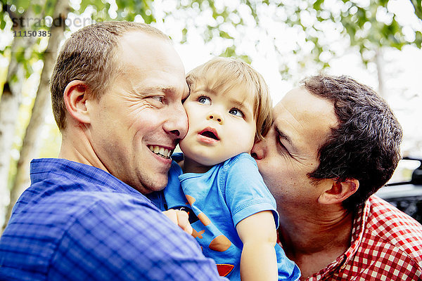 Schwule Väter küssen ihren kleinen Sohn im Freien