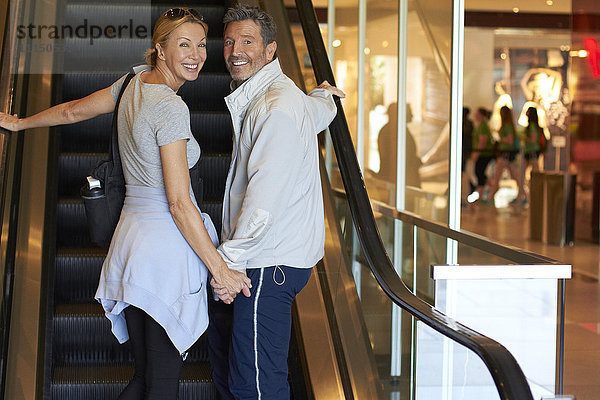 Kaukasisches Paar auf Rolltreppe in Einkaufszentrum