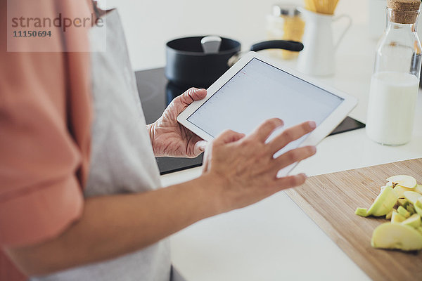 Ältere kaukasische Frau benutzt digitales Tablet in der Küche