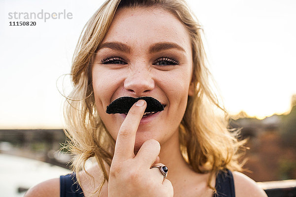 Kaukasisches Teenager-Mädchen spielt mit falschem Schnurrbart