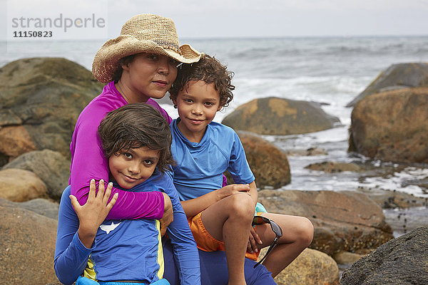 Mutter und Kinder umarmen sich am felsigen Strand