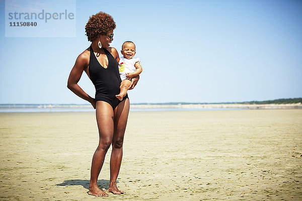 Lächelnde Mutter hält Mädchen am Strand
