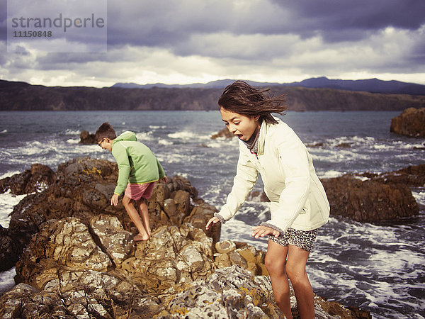 Gemischtrassiger Bruder und Schwester spielen am felsigen Strand