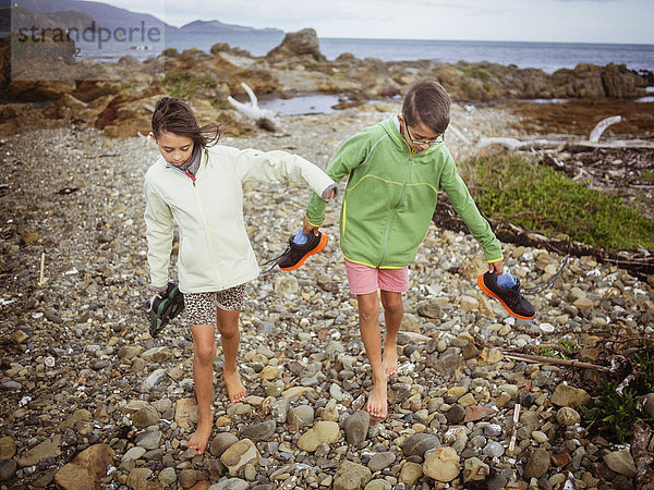 Gemischtrassiger Bruder und Schwester tragen ihre Schuhe am felsigen Strand