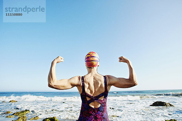 Ältere kaukasische Frau  die ihre Muskeln am Strand anspannt