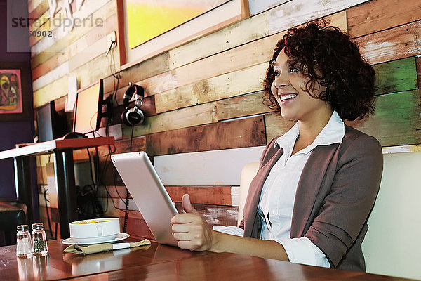 Gemischtrassige Frau benutzt Tablet-Computer in einem Café