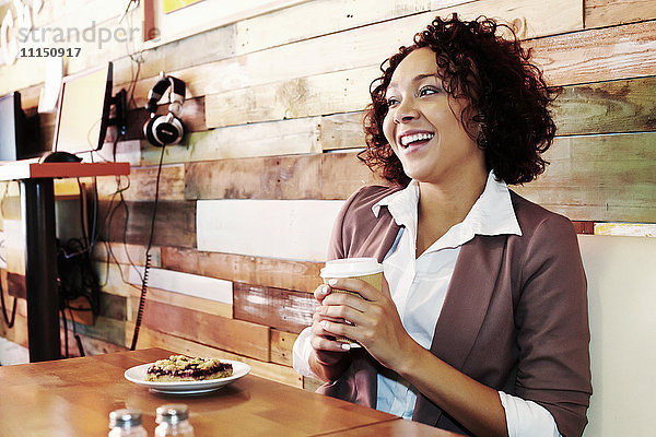 Gemischtrassige Geschäftsfrau mit Kaffee und Gebäck in einem Cafe