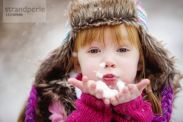 Kaukasisches Mädchen bläst eine Handvoll Schnee
