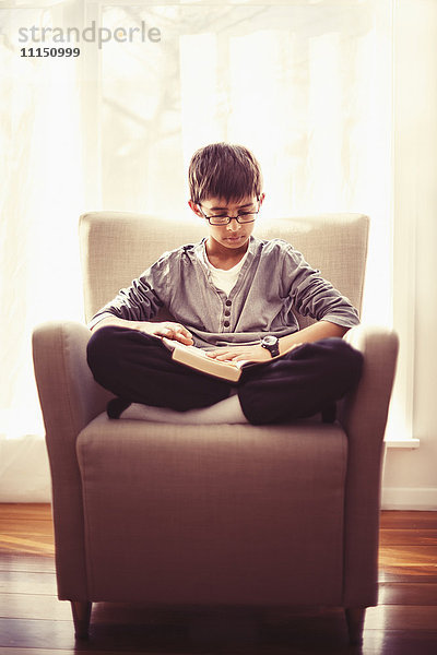 Gemischtrassiger Junge  der im Sessel ein Buch liest