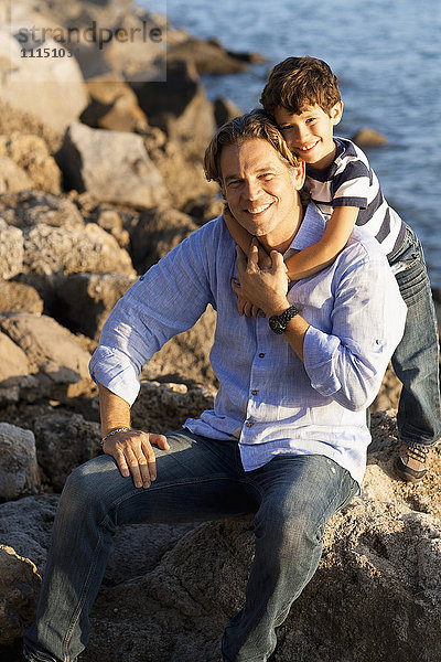 Kaukasischer Vater und Sohn umarmen sich am felsigen Strand