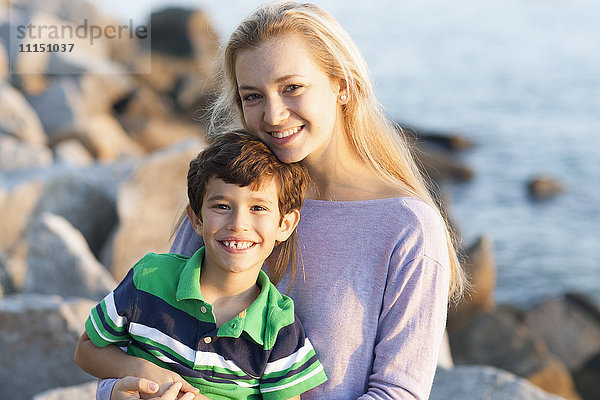 Kaukasischer Bruder und Schwester lächelnd am felsigen Strand