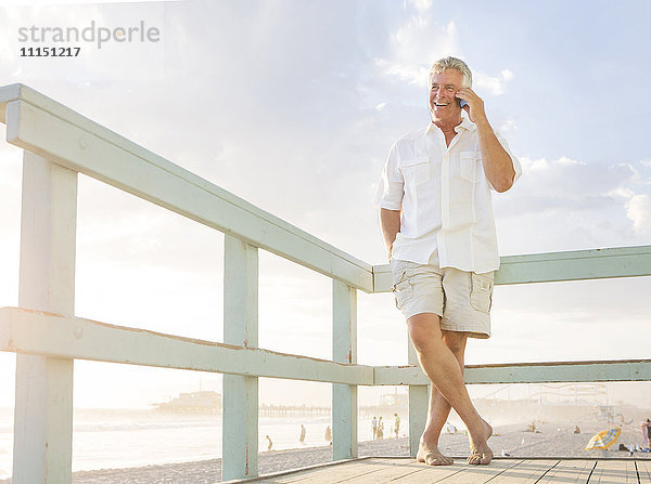 Kaukasischer Mann  der an der Strandpromenade mit seinem Handy telefoniert