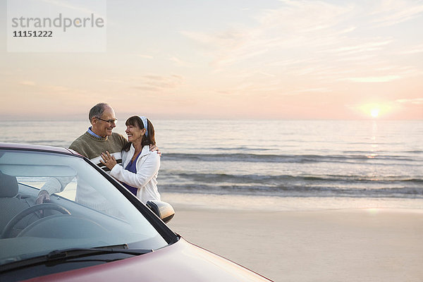 Älteres Paar steht am Auto am Strand