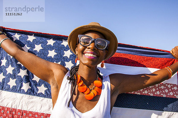 Schwarze Frau hält amerikanische Flagge unter blauem Himmel