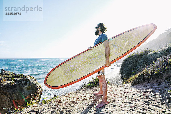 Kaukasischer Mann hält Surfbrett am Strand