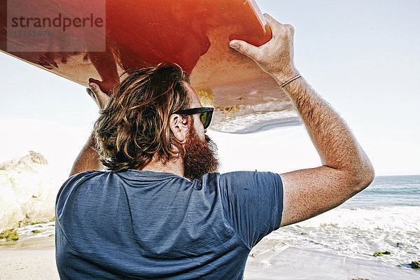 Kaukasischer Mann hält Surfbrett am Strand