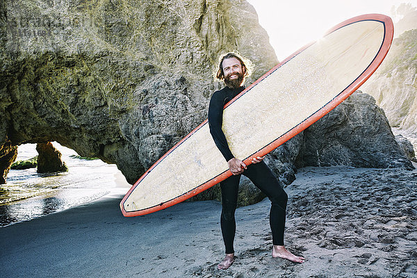 Kaukasischer Mann hält Surfbrett am Strand