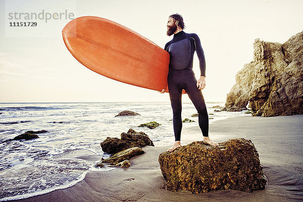 Kaukasischer Mann hält Surfbrett am Strand