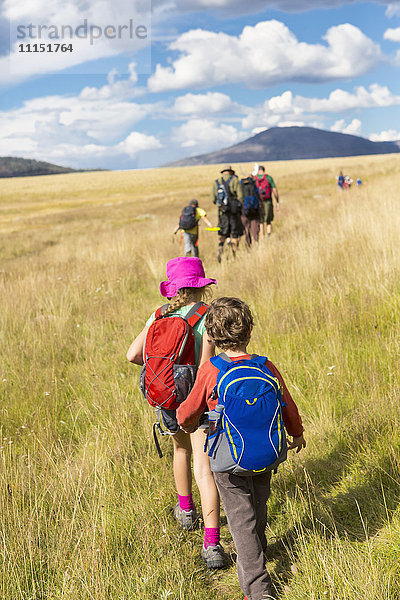 Kaukasische Kinder  die auf einer Wiese in einer abgelegenen Landschaft spazieren gehen