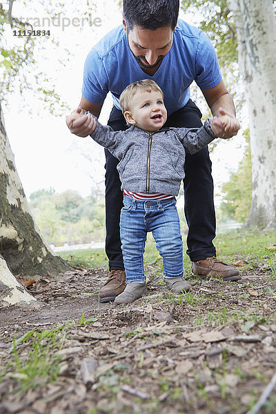 Kaukasischer Vater hilft seinem kleinen Sohn beim Laufen im Freien