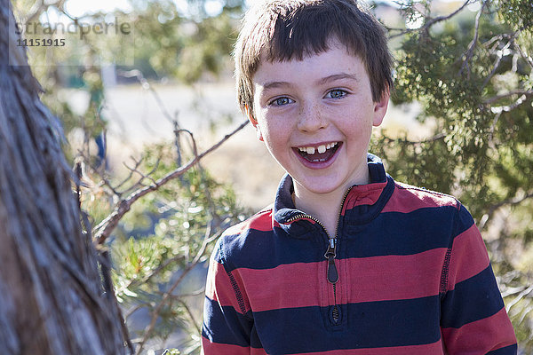 Nahaufnahme eines lächelnden kaukasischen Jungen in der Nähe eines Baumes