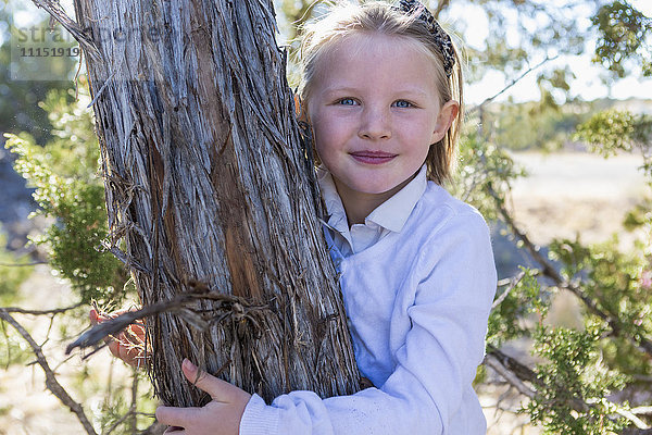 Lächelndes Mädchen  das einen Baum umarmt