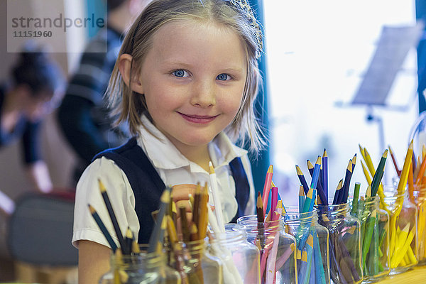 Gemischte Rasse Mädchen lächelnd in der Nähe multicolor Bleistifte im Klassenzimmer